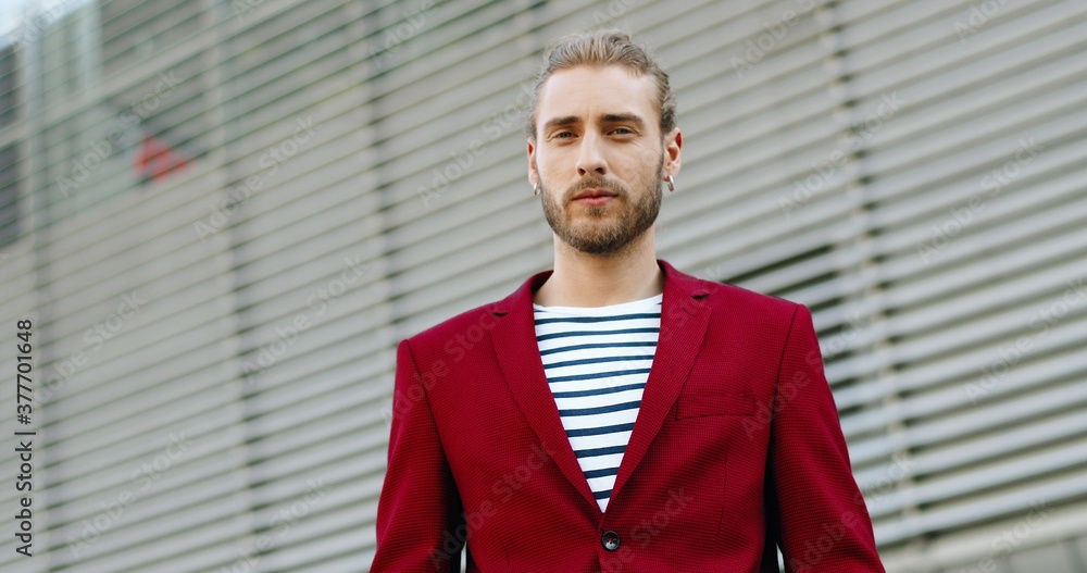 Portrait shot of Caucasian young handsome man in red jacket looking at camera and smiling cheerfully outdoor. Stylish joyful good-looking guy at building outside. Portrait shot of Caucasian young handsome man in red jacket looking at camera and smiling cheerfully outdoor. Stylish joyful good-looking guy at building outside.