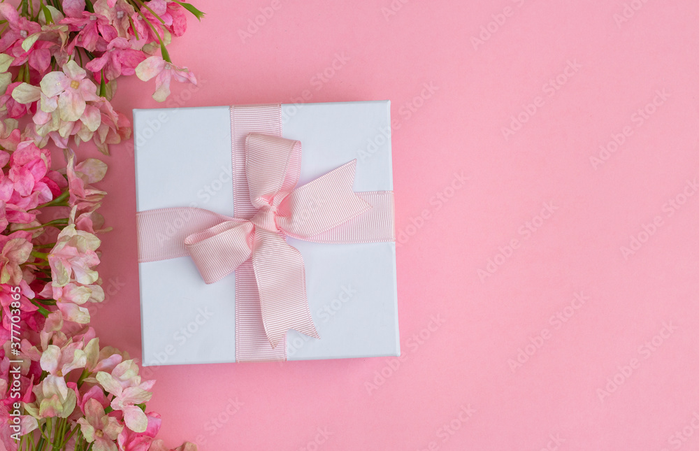 Pink flowers and a gift box on pink background. Space for text