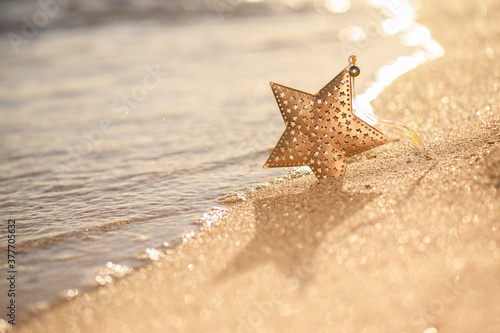 Fototapeta Naklejka Na Ścianę i Meble -  Christmas gold star decoration on the beach on a seascape backgound, summer Christmas and winter holyday concept, selective focus. Merry Christmas and Happy New Year background
