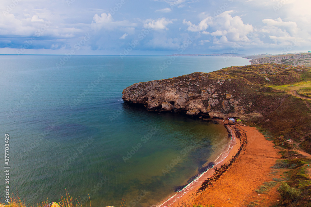 Obraz premium Landscape of the morning sea coast. The turquoise surface of the calm sea. Picturesque dark clouds in the blue sky. Picturesque coastal cliffs. Tourism and travel.