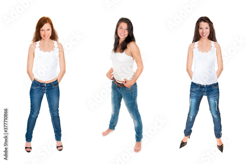 Full length portraits of three attractive young women wearing blue jeans an bright tops, isolated on white studio background