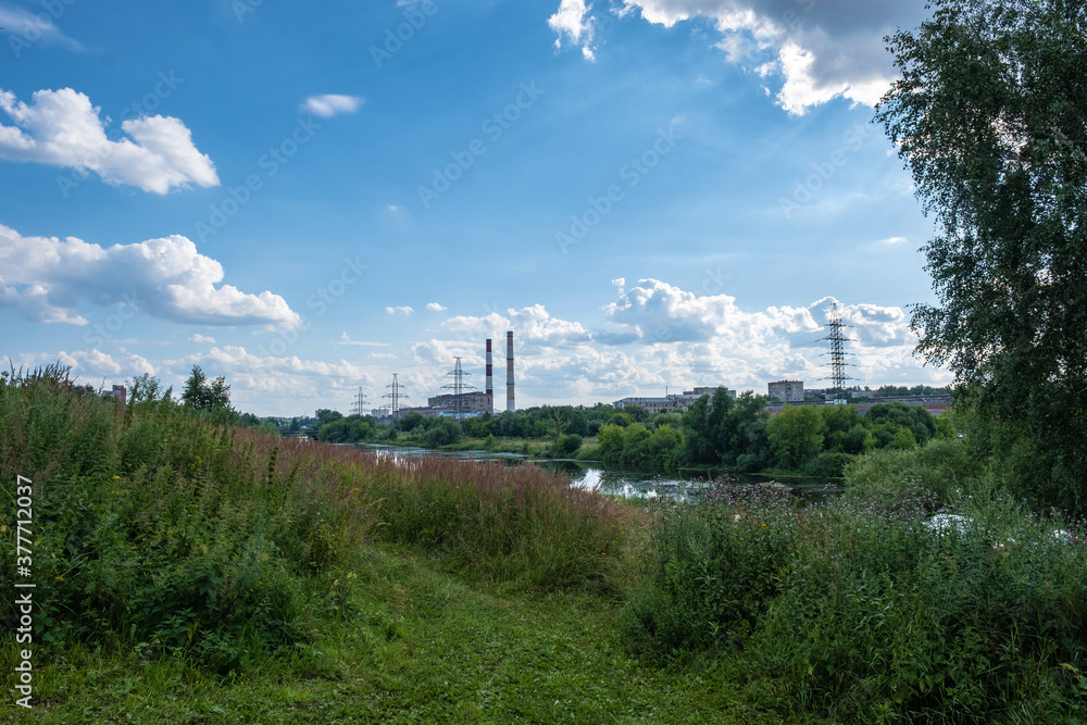 City landscape with the Uvod river with a power line and high pipes on a sunny summer day.