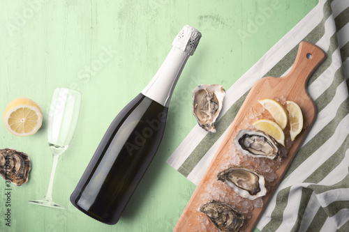 An unopened champagne bottle with a single glass on a green tinted wooden background with fresh oysters and lemon on a wooden cutting board photo