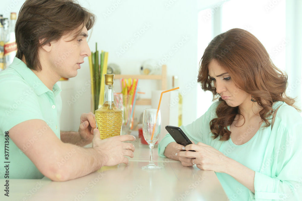 Upset young woman texting on smartphone and waiting for drink Upset young woman texting on smartphone and waiting for drink
