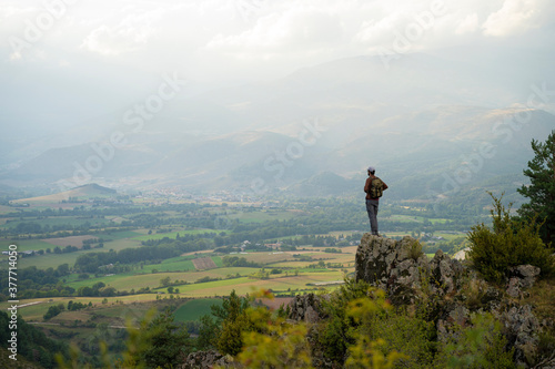 Thoughtful young man trekking or hiking on a cliff looking at the mountains. Beautiful landscape and a solitary man. Nature's vastness, freedom, inspiration. Outdoor adventure.