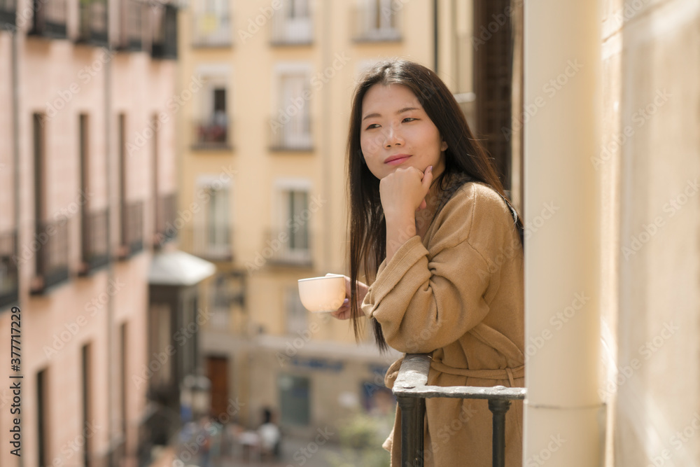 young happy and beautiful Asian Japanese woman enjoying city view from hotel room balcony in Spain during holidays trip in Europe drinking coffee smiling cheerful