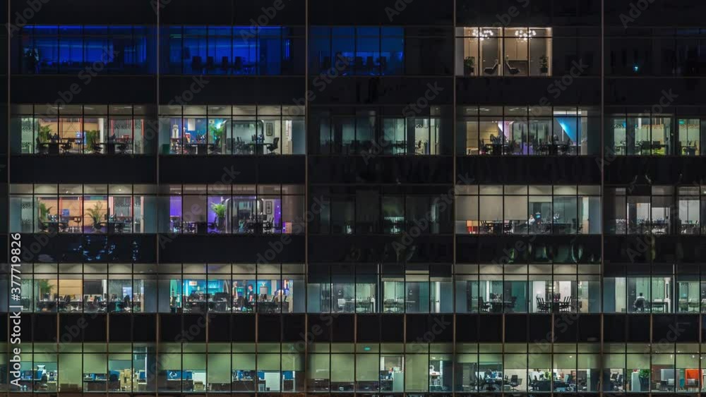 Modern office building with big windows at night timelapse close up view, in windows glowing light shines and some people inside, Singapore Modern office building with big windows at night timelapse close up view, in windows glowing light shines and some people inside, Singapore