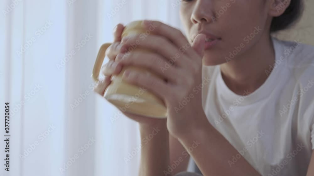 Close up tan Asian female holding coffee mug, wake up early for morning coffee, sit down alone inside the house, drinking hot beverage, hot tea caffeine addicted, natural day light from The window Close up tan Asian female holding coffee mug, wake up early for morning coffee, sit down alone inside the house, drinking hot beverage, hot tea caffeine addicted, natural day light from The window