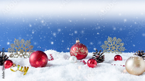 Christmas ornaments on snow over blue background with snowflakes.