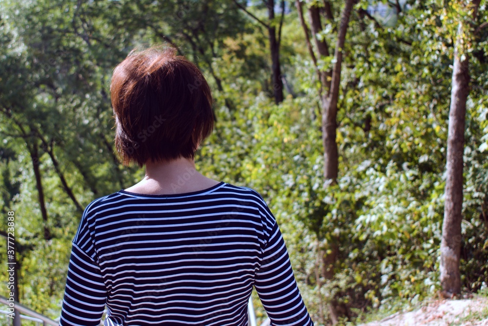 Fototapeta premium girl in striped T-shirt on blurred background of green forest. view from the back