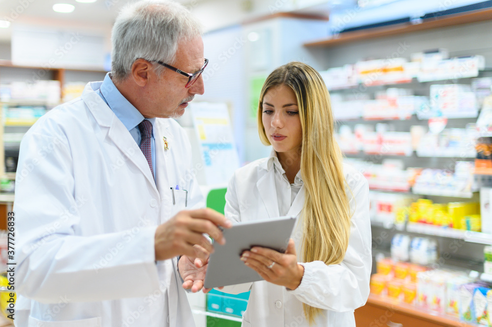 Obraz premium Two pharmacists talking while working on tablet in their store