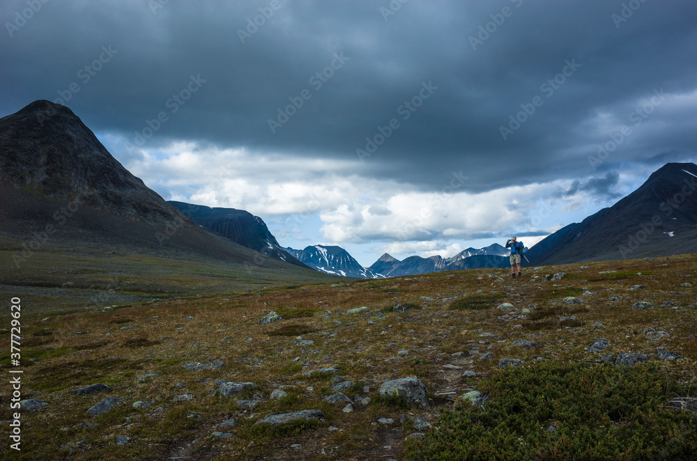 Hiking in Swedish Lapland. Man trekking alone in northern Sweden in Stuor Reaiddavaggi valley. Arctic mountain nature of Scandinavia in summer cloudy day