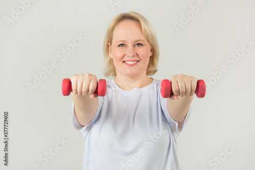 beautiful young plump woman in a white t-shirt on a white background with dumbbells