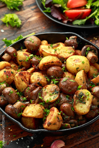 Baked potato with mushrooms and herbs in iron cast pan on wooden table