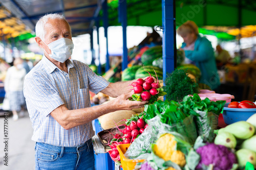retired european man wearing medical mask protecting against the virus buying radishes and cabbage in market photo