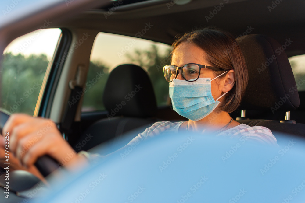 Beautiful young happy woman driving her new car in protective sterile medical mask at sunset. Beautiful young happy woman driving her new car in protective sterile medical mask at sunset.