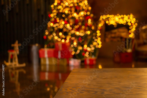 Dark Christmas and New year background with empty dark wooden table over christmas tree and blurred light bokeh. Empty display for product montage. Rustic vintage Xmas background.