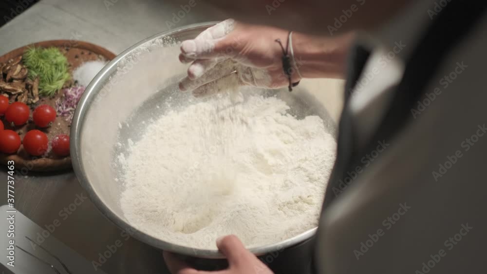 The cook mixing flour with his hand, saturating it with oxygen. Vegetables in the background. 4k. Slow motion The cook mixing flour with his hand, saturating it with oxygen. Vegetables in the background. 4k. Slow motion