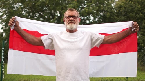 Protests in Belarus. A mature man with a gray beard and glasses holds a Belarusian red-white flag, the situation in Belarus photo