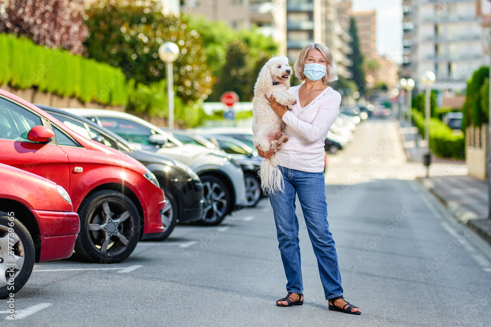 Mature woman walking with a dog outdoors an antivirus mask