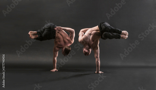 two twin brothers in black jeans with a naked torso perform acrobatic elements, black background 