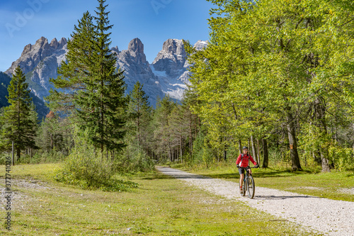 nice and active senior woman riding her electric mountain bike on an old railway embankment in the Hoehlenstein valley  between Toblach and Cortina Dampezzo, Three Peaks Dolomites, South Tirol, Italy