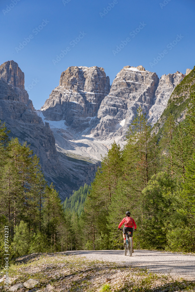 nice and active senior woman riding her electric mountain bike on an old railway embankment in the Hoehlenstein valley  between Toblach and Cortina Dampezzo, Three Peaks Dolomites, South Tirol, Italy