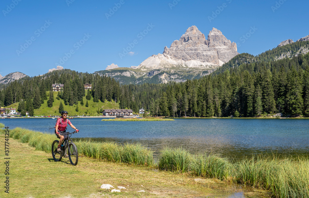 nice senior woman ridung her electric mountain bike at the shore of Misurina Lake below the famous summits of the Three peak of Lavaredo in the Dolomites mountains in South Tirol, Italy