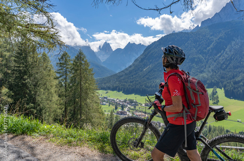 pretty senior woman riding her electric mountainbike in the Fischlein Valley in the Sexten Dolomites wit famous Sextan sundial in background, Tre cime National park, South Tirol, Italy  photo