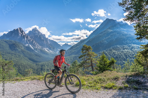 nice and active senior woman riding her electric mountain bike on a old military road from Toblach upt to the summit of Marchkinkele eith spectacular view to the Three peaks of Lavaredo, South Tirol, 