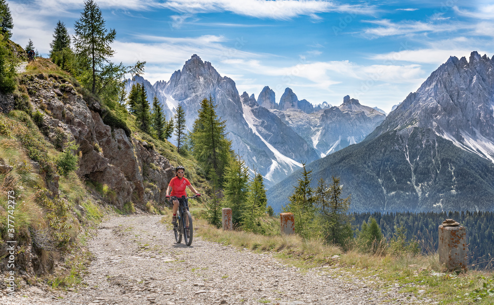 nice and active senior woman riding her electric mountain bike on a old military road from Toblach upt to the summit of Marchkinkele eith spectacular view to the Three peaks of Lavaredo, South Tirol, 