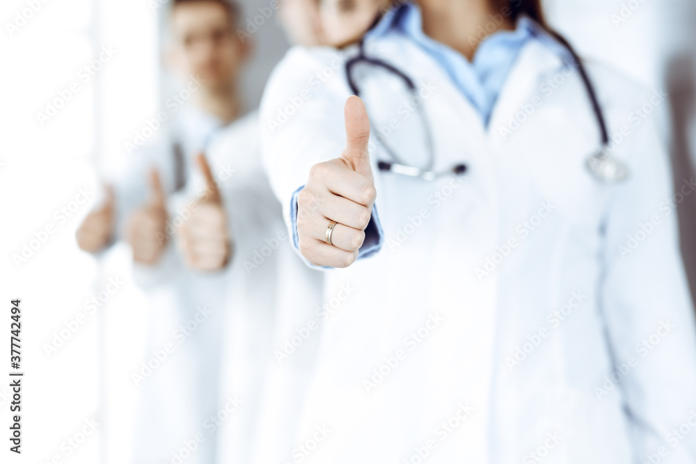 Group of modern doctors standing as a team with thumbs up in hospital office. Medical help, insurance in health care, best desease treatment and medicine concept Group of modern doctors standing as a team with thumbs up in hospital office. Medical help, insurance in health care, best desease treatment and medicine concept
