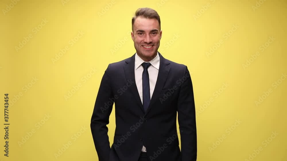 handsome businessman standing wiht one hand in pocket, looking down, moving his look at the camera, smiling and crossing his arms on yellow background handsome businessman standing wiht one hand in pocket, looking down, moving his look at the camera, smiling and crossing his arms on yellow background
