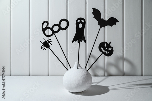 Halloween home decorations. Painted white pumpkin and black Halloween scary shadow puppets on sticks against a white wooden wall. Copy space