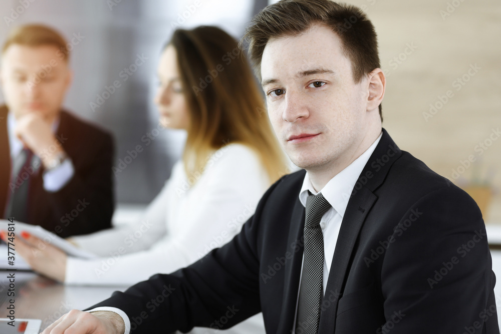Fototapeta premium Businessman headshot at meeting in sunny office. Unknown entrepreneur sitting with colleagues at the background