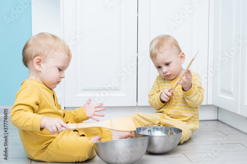 Twin boys play in the kitchen with kitchenware.