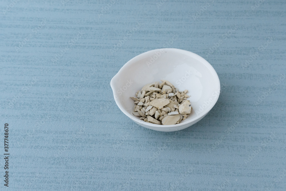 White clay powder lie in white bowl isolated on blue background. Ural food clay. top view. no people. copy space White clay powder lie in white bowl isolated on blue background. Ural food clay. top view. no people. copy space