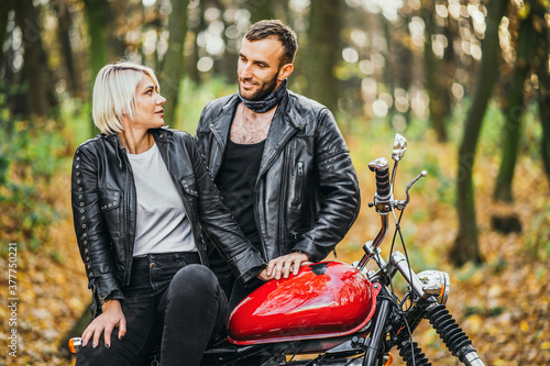 Pretty couple near red motorcycle on the road in the forest with colorful blured background