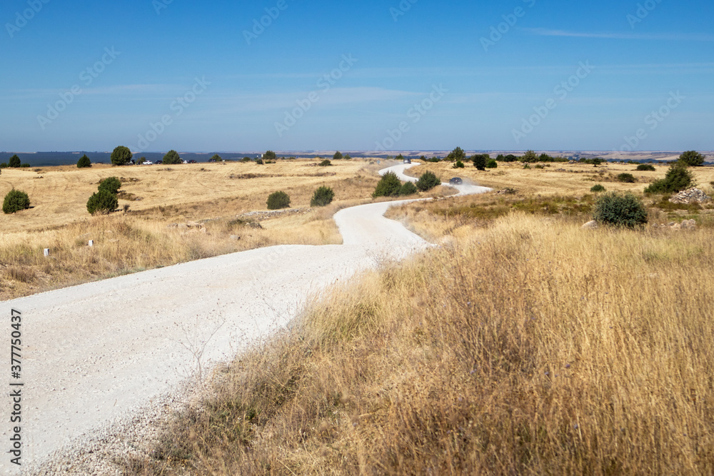 Obraz premium Rural road in the Spanish countryside among agricultural fields, after wheat harvest season. Cars driving on a dusty unsealed road. Summer time in the dry Spanish outback. Soria, near Madrid, Spain