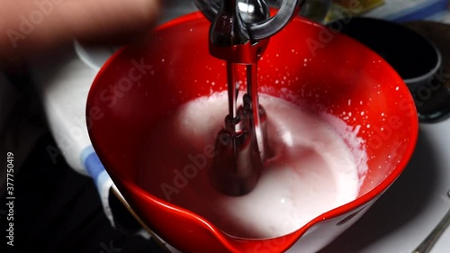 A whisk is used to make whipped cream in a red bowl photo