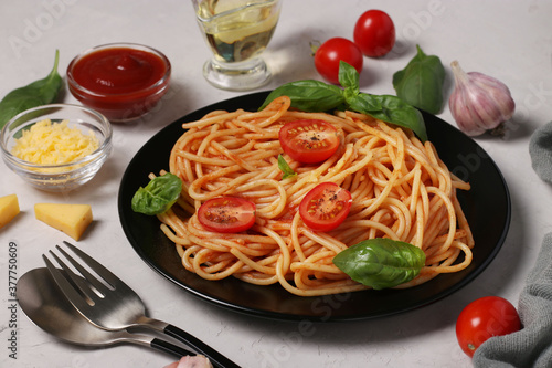 Spaghetti with tomato sauce and cherry tomatoes with basil on black plate on light background, Closeup