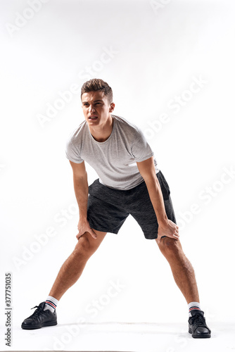 A sports man in shorts and a full-length T-shirt does exercises on a light background © SHOTPRIME STUDIO
