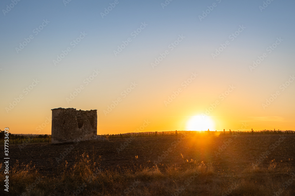 Abandoned old tower in the Spanish countryside at sunset time. Sun hiding behind a wheat field after harvesting season. Summer time, dry hot weather. Editing space. Sebúlcor, Soria, near Madrid, Spain