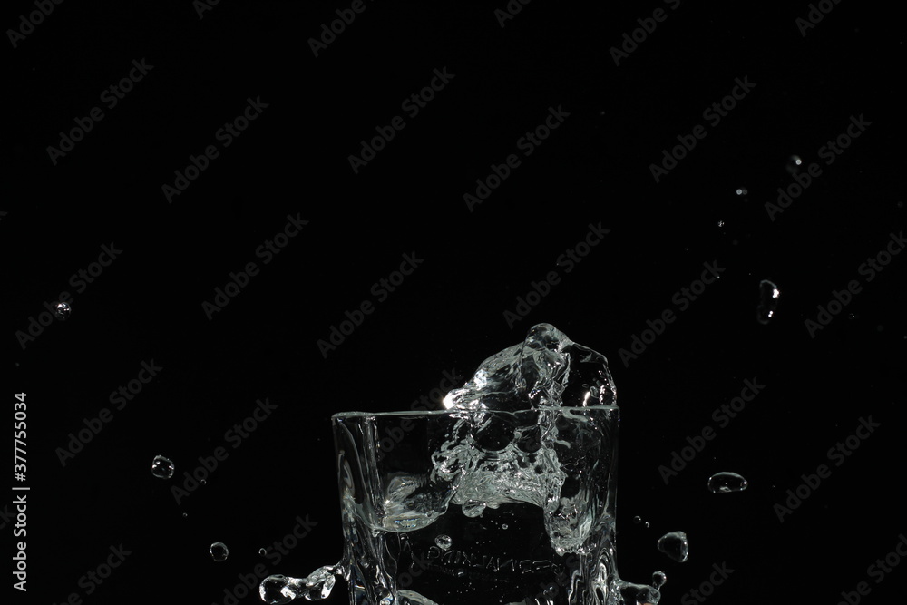 splash of water in a glass by ice cube on black background splash of water in a glass by ice cube on black background