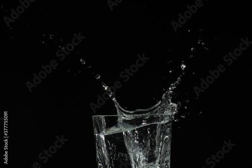 splash of water in a glass by ice cube on black background