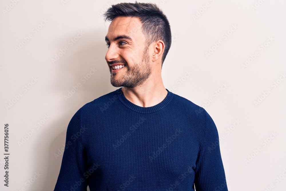 Young handsome man with beard wearing casual sweater standing over white background looking to side, relax profile pose with natural face and confident smile. Young handsome man with beard wearing casual sweater standing over white background looking to side, relax profile pose with natural face and confident smile.
