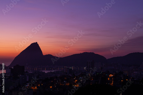 Beautiful distant view of the Sugar Loaf mountain silhouette at sunset against purple sky; Rio de Janeiro, Brazil. Some of the Rio de Janeiro City in the foreground. Copy space for text.