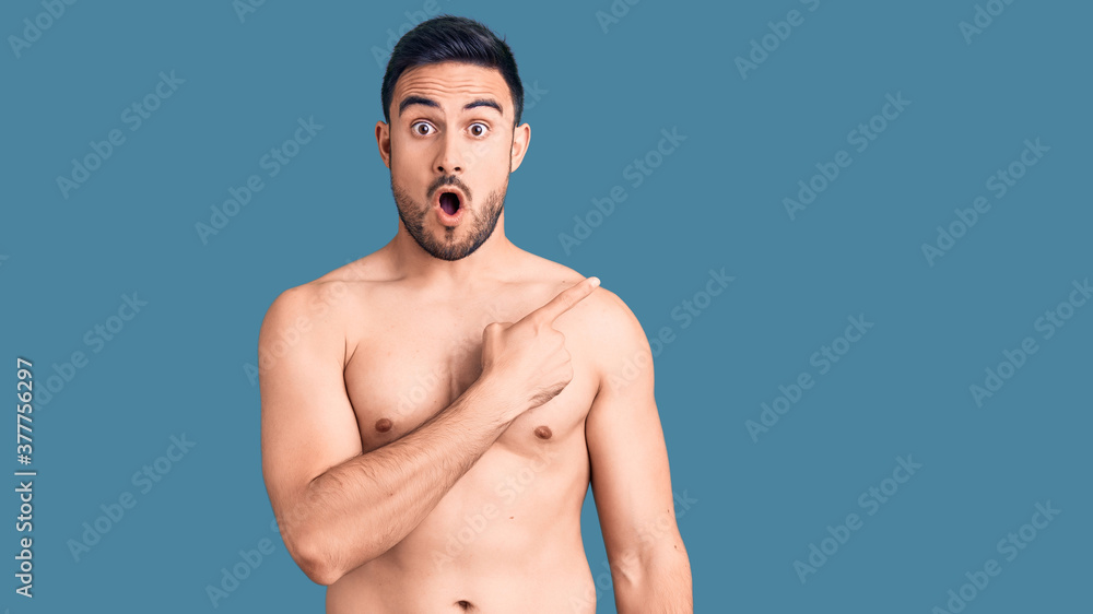 Fototapeta premium Young handsome man wearing swimwear surprised pointing with finger to the side, open mouth amazed expression.