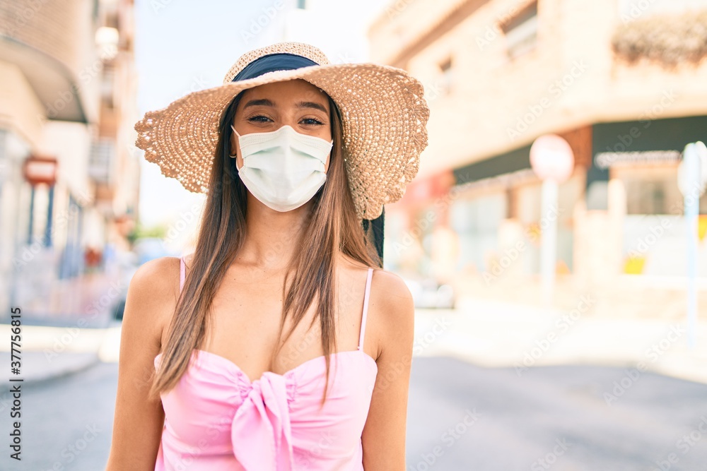 Young hispanic woman on vacation wearing medical mask walking at street of city