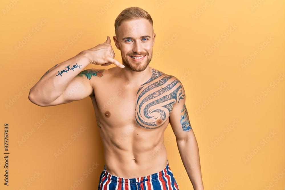 Young caucasian man wearing swimwear shirtless smiling doing phone gesture with hand and fingers like talking on the telephone. communicating concepts.